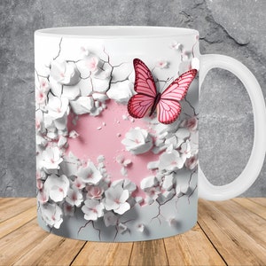 Pode incluir: Caneca de cerâmica branca com um design floral rosa e branco e uma borboleta rosa. O design parece estar rachado e quebrado, com a borboleta emergindo das rachaduras.
