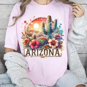 May include: Pink t-shirt featuring a watercolour design of a cactus, flowers, and the text "ARIZONA".