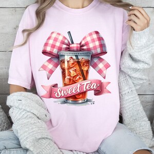 May include: Pink t-shirt with a graphic of a glass of iced tea with a pink and white gingham bow and the text "Sweet Tea".