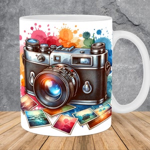 May include: White ceramic mug with a vintage camera illustration and watercolor-style splashes of color. The camera is surrounded by instant photos with various landscapes.
