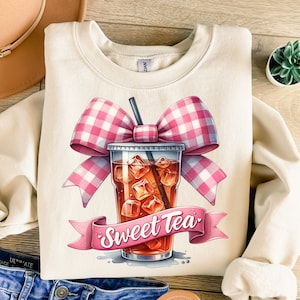 May include: A beige sweatshirt with a graphic of a pink and white gingham bow on top of a glass of iced tea with the text "Sweet Tea".