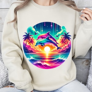May include: A cream-colored sweatshirt with a colorful graphic of two dolphins jumping over a sunset ocean scene. The graphic includes palm trees, stars, and a rainbow-colored wave.