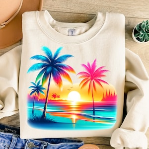 May include: A beige sweatshirt with a colorful sunset and palm trees graphic print. The graphic features a bright orange sun, blue water, and palm trees with rainbow colored leaves.