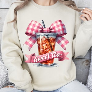 May include: A beige sweatshirt with a pink and white gingham bow on top of a glass of iced tea with the text "Sweet Tea" on a pink ribbon.