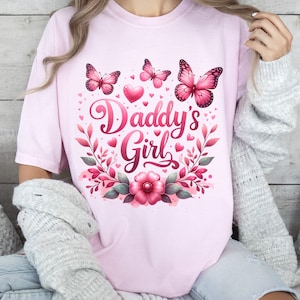 May include: Pink t-shirt with a floral design and butterflies. The text "Daddy's Girl" is written in a decorative font.