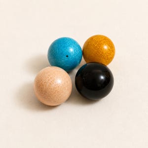 May include: Four spherical beads arranged in a cluster. One bead is bright turquoise with a visible hole, one is a textured mustard yellow, one is a light beige with a natural wood grain pattern, and one is a smooth, glossy solid black sphere.