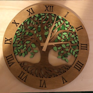 May include: A wooden clock with a tree of life design. The clock face features Roman numerals and the tree is carved with green leaves.