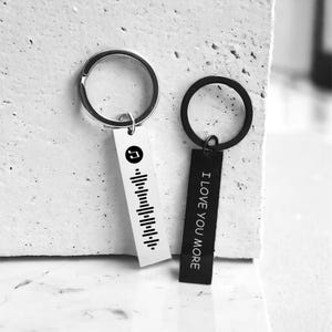 May include: Two silver keyrings with black rectangular tags. One tag has a music note and a barcode, the other says "I Love You More".