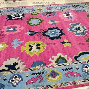 May include: A pink rug with a blue, green, and white geometric pattern. The rug has a border with a similar pattern.