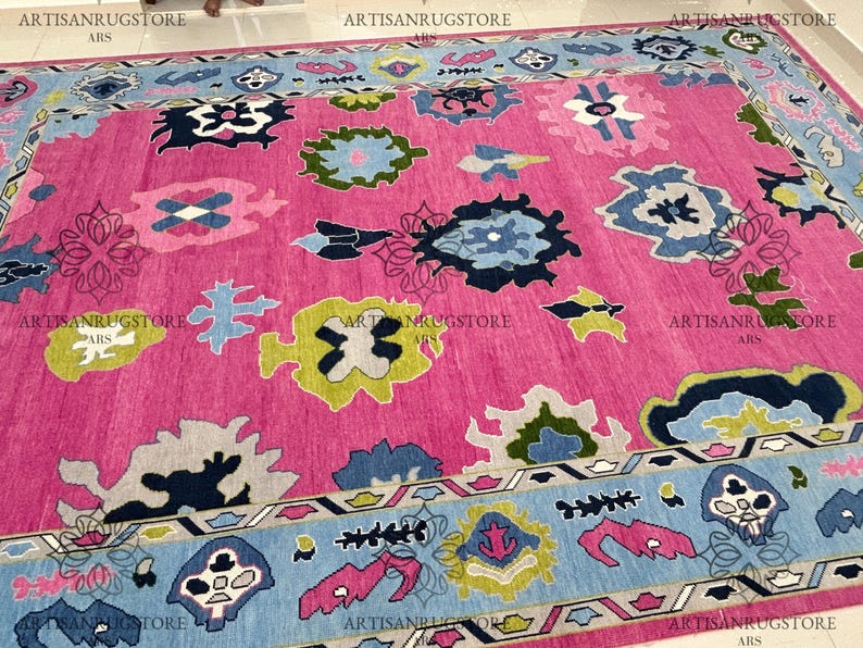 May include: A pink rug with a blue, green, and white geometric pattern. The rug has a border with a similar pattern.