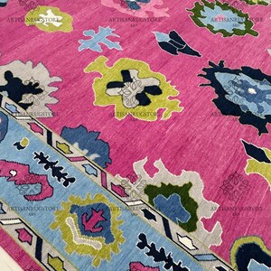 May include: A pink rug with a blue, green, and yellow geometric pattern. The rug has a border with a repeating pattern of triangles and zigzags.