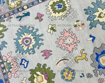 Può includere: Un tappeto grigio con un motivo geometrico colorato. Il motivo presenta forme blu, rosa, verdi e gialle. Il tappeto ha una leggera lucentezza e una texture morbida.
