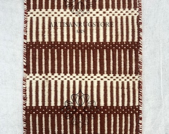 May include: A rectangular rug with a repeating pattern of vertical brown stripes alternating with off-white stripes. The rug has a fringed edge and the text "ARTISAN RUGSTORE ARS" is visible. A tag with the text "PR-22" is attached to the rug.