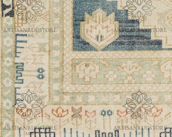 May include: Close-up of a beige rug with a blue and white geometric pattern. The rug has a fringe border and is made of wool. The rug is in good condition and has a vintage look.
