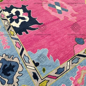 May include: A pink, blue, and green patterned rug with a geometric design. The rug has a fringe border and is made of wool.
