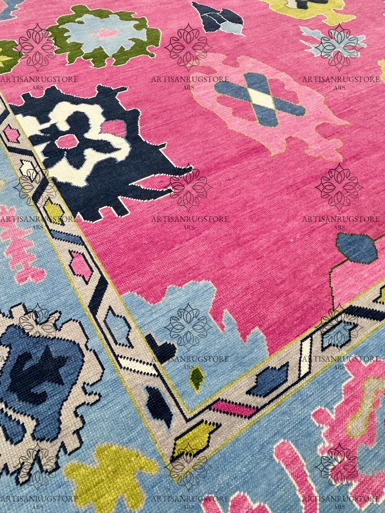 May include: A pink, blue, and green patterned rug with a geometric design. The rug has a fringe border and is made of wool.