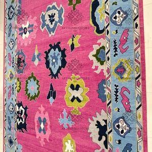 May include: A pink rug with a colorful geometric pattern. The rug has a blue, green, yellow, and white design. The rug has a border with a geometric pattern.