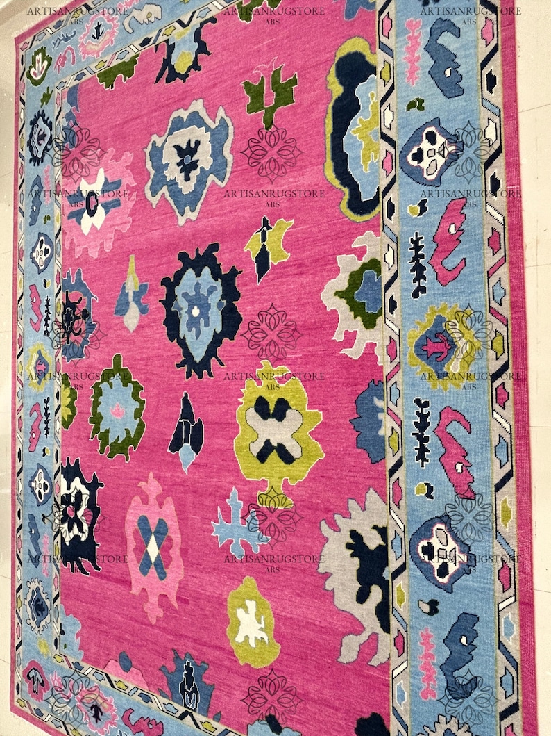 May include: A pink rug with a colorful geometric pattern. The rug has a blue, green, yellow, and white design. The rug has a border with a geometric pattern.