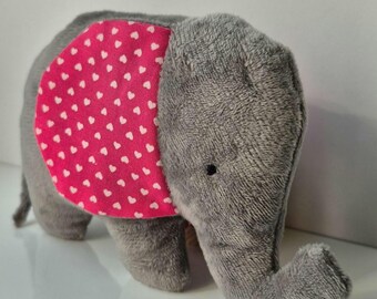 Può includere: Un giocattolo di peluche di elefante grigio con un orecchio rosa con motivo a forma di cuore.