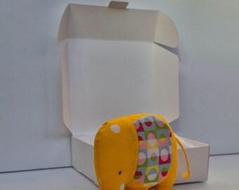 Può includere: Un giocattolo di elefante di stoffa giallo con pois bianchi e un motivo geometrico colorato sulla schiena. L'elefante è in piedi su una superficie bianca.