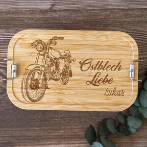 Könnte beinhalten: Eine Holzlunchbox mit einem Vintage-Motorrad-Design und dem Text "Ostblech Liebe Lukas" auf der Vorderseite.