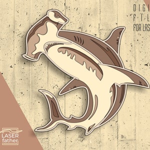 May include: A digital file for laser cutting a hammerhead shark design. The shark is outlined in black and has a layered design with different shades of brown and beige.