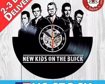 Könnte beinhalten: Schwarze Schallplattenuhr mit einer Silhouette der Band New Kids on the Block. Die Uhr hat ein silbernes Zifferblatt mit schwarzen Zahlen und Zeigern. Die Uhr ist auf einem schwarzen Hintergrund montiert.
