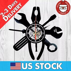 May include: Black vinyl record clock with a design of various tools, including wrenches, screwdrivers, and pliers. The clock has a silver face with black numbers and hands. The clock is mounted on a black background.