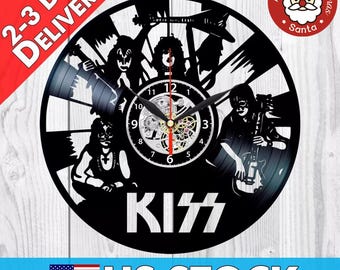 Könnte beinhalten: Schwarz-weiße Schallplattenuhr mit einer Silhouette der Band KISS. Das Zifferblatt der Uhr hat römische Ziffern und ein Uhrwerk mit freiliegenden Zahnrädern. Der Name der Band ist in großen weißen Buchstaben unter dem Zifferblatt geschrieben.