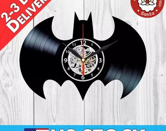 Könnte beinhalten: Eine schwarze Schallplattenuhr in Form des Batman-Logos. Das Zifferblatt der Uhr ist silberfarben mit schwarzen Zeigern und einem schwarzen und goldenen Getriebemechanismus. Die Uhr ist auf einer weißen Holzoberfläche montiert.