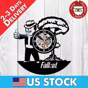 May include: Black and white vinyl record clock featuring a Fallout character with a mushroom cloud behind them. The clock face is a silver skeleton clock with black numbers. The clock has the word "Fallout" printed below the character.