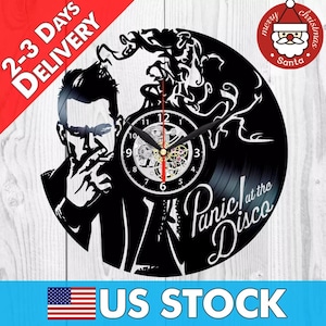 May include: Black vinyl record clock featuring a silhouette of a person smoking with the text "Panic! at the Disco" in white lettering.