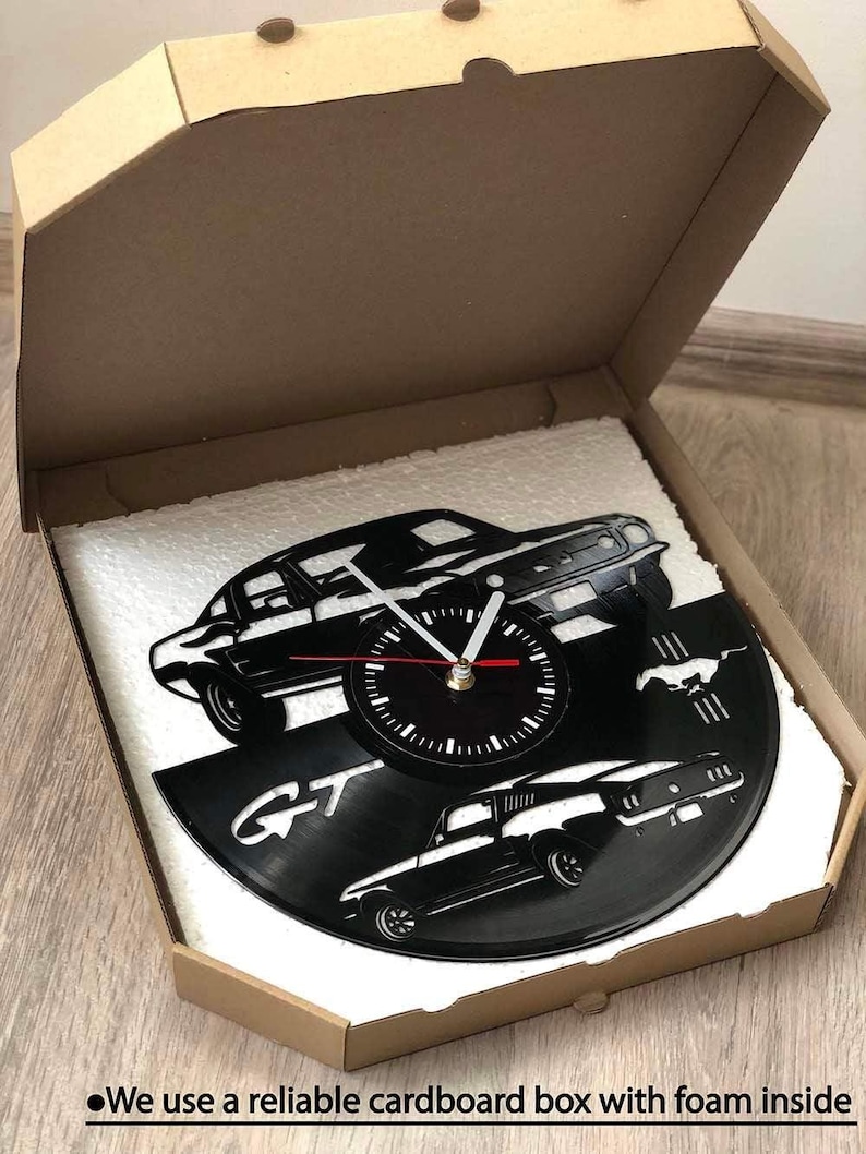 K&ouml;nnte beinhalten: Schwarze Vinyl-Schallplattenuhr mit einem klassischen Autodesign und den Buchstaben "GT". Die Uhrzeiger sind wei&szlig; und rot. Die Uhr ist in einem Karton mit Schaumstoffpolster verpackt. Der Text auf der Box lautet "We use a reliable cardboard box with foam inside."