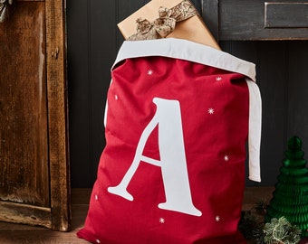 May include: Red Christmas gift sack with a white letter A printed on the front. The sack has a white trim and is decorated with white snowflakes.