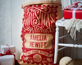 May include: A red and white personalized Christmas sack with the text "Christmas Wishes Amelia Hewitt" and "If lost please return to The North Pole Workshop".