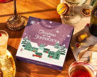 Può includere: Una scatola viola con un'illustrazione di scena invernale e il testo "Christmas at the Johnson's" e "Mayfair Chocolatier".