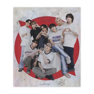 May include: A group of people are posing for a photo on a white blanket. The background features a red circle and a white background. The people are wearing casual clothing, including t-shirts and jeans. Some of them are making heart shapes with their hands.
