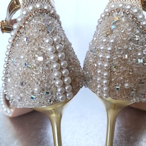 May include: A pair of gold high-heeled sandals with a delicate mesh fabric upper adorned with pearl and crystal embellishments.