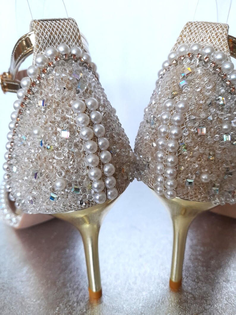May include: A pair of gold high-heeled sandals with a delicate mesh fabric upper adorned with pearl and crystal embellishments.