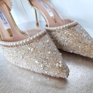 May include: A pair of ivory bridal heels with a pointed toe and a delicate pearl and crystal embellishment. The heels have a gold stiletto.