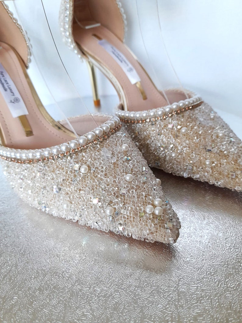 May include: A pair of ivory bridal heels with a pointed toe and a delicate pearl and crystal embellishment. The heels have a gold stiletto.