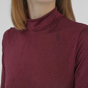 Puede incluir: Una camiseta de cuello alto de manga larga de color burdeos, hecha de una tela suave y texturizada.