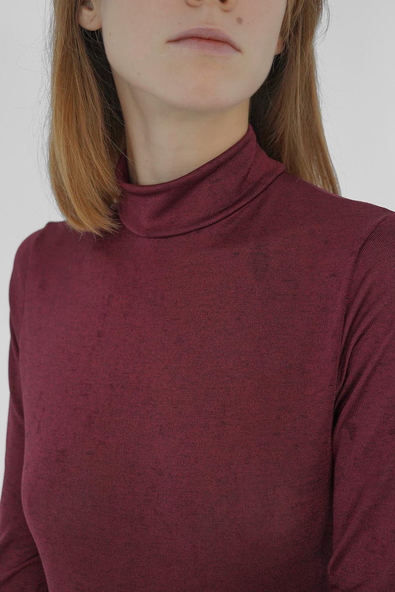 Puede incluir: Una camiseta de cuello alto de manga larga de color burdeos, hecha de una tela suave y texturizada.