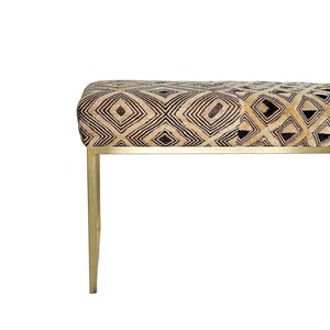 May include: A bench with a geometric patterned seat in shades of tan, black, and gold. The bench has a rectangular seat and is supported by gold-colored metal legs. The design features diamond and square shapes.