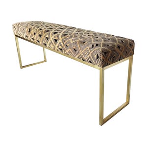 May include: A rectangular bench with a geometric patterned seat in black, tan, and gold. The bench has a gold metal frame. The seat cushion features a repeating diamond and square design.