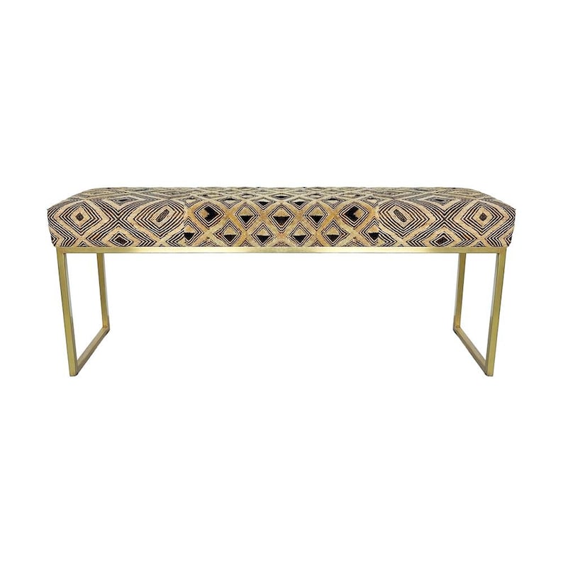 May include: A rectangular bench with a patterned top and gold-colored metal legs. The bench top features a geometric design in black, tan, and cream colors. The legs are a simple, modern design.