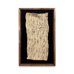 May include: Abstract artwork in a dark wooden frame. The artwork features a beige, textured paper with black, linear markings and shapes. The background is black, and the frame is a warm brown.