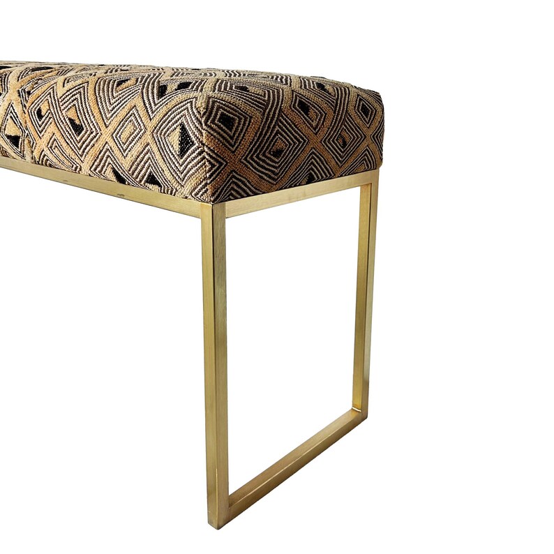 May include: A rectangular bench with a geometric patterned top in shades of gold, black, and brown. The bench has a gold-colored metal frame. The design features a repeating diamond pattern.