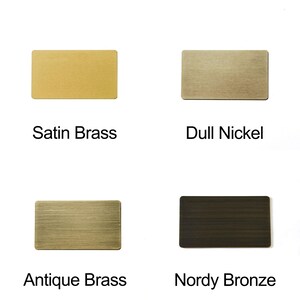 May include: Four rectangular metal samples in different finishes: Satin Brass, Dull Nickel, Antique Brass, and Nordy Bronze. Each sample has a brushed texture and is labeled with its finish name in black text.
