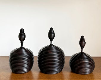 Op de afbeelding: Drie decoratieve houten dozen met een donkerbruine afwerking. Elke doos heeft een afgeronde bovenkant met een gelaagd, geribbeld ontwerp en een klein, puntig torentje.